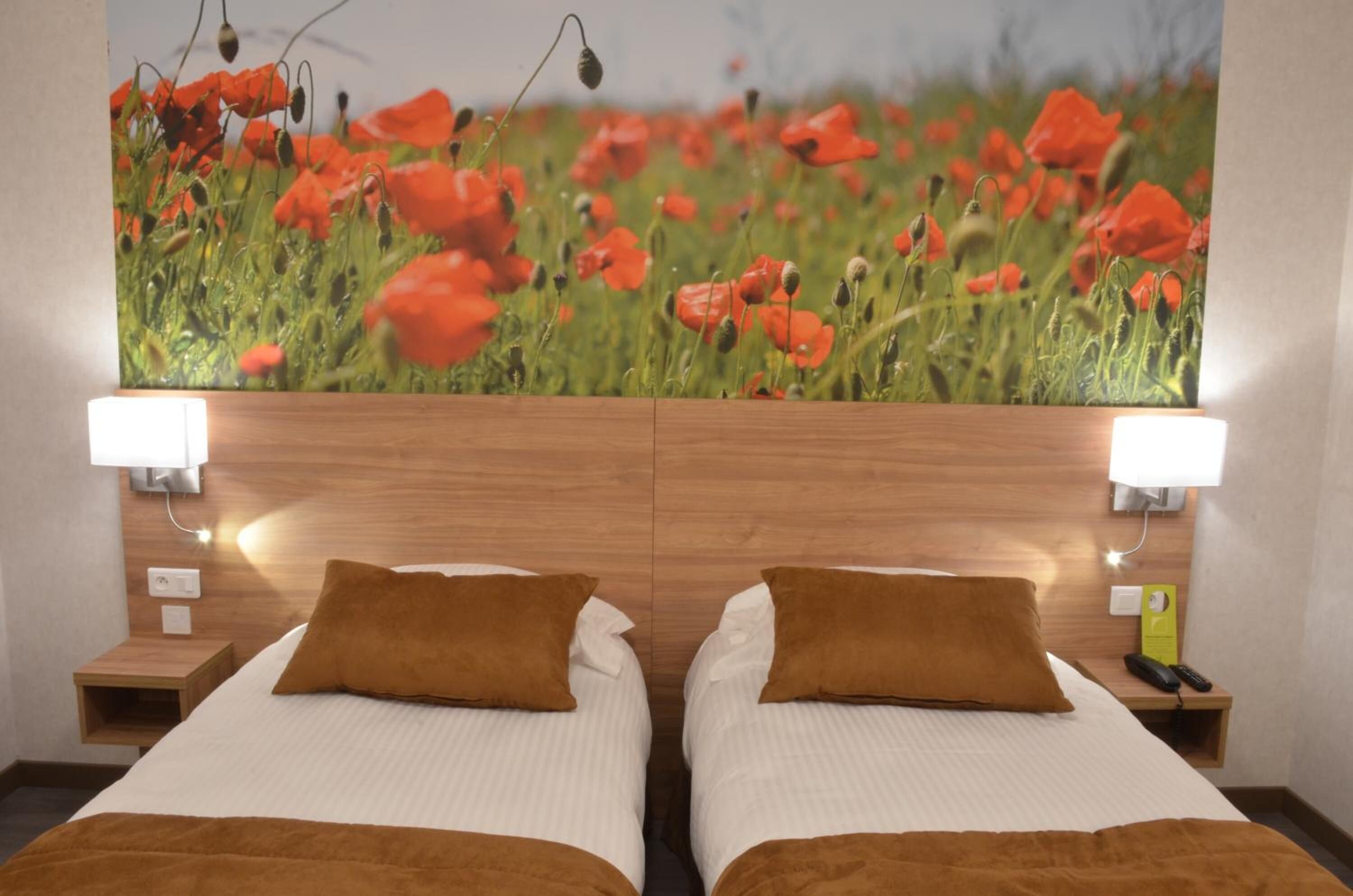 A hotel room with two beds, wooden headboard, bedside lamps, and a large poppy flower wall art.