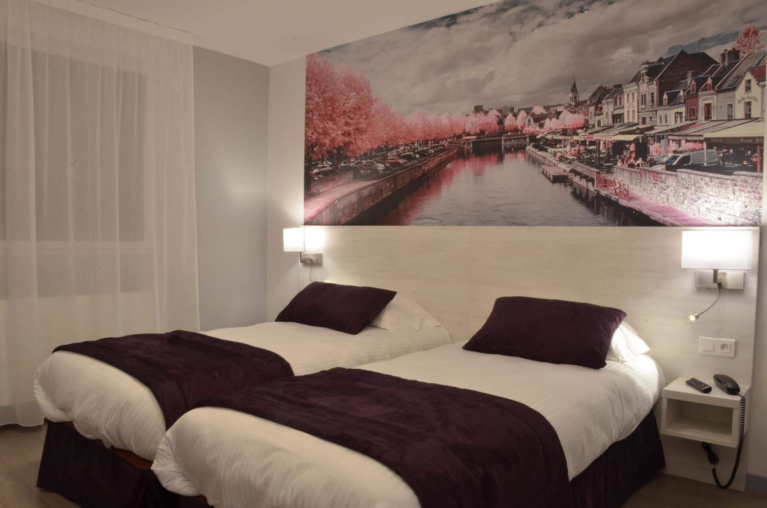 A hotel room with two beds, a large window with sheer curtains, a wall-mounted painting of a river scene, and bedside lamps.