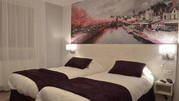 Une chambre d’hôtel avec deux lits, une grande fenêtre avec des rideaux légers, un tableau représentant un paysage fluvial accroché au mur et des lampes de chevet.