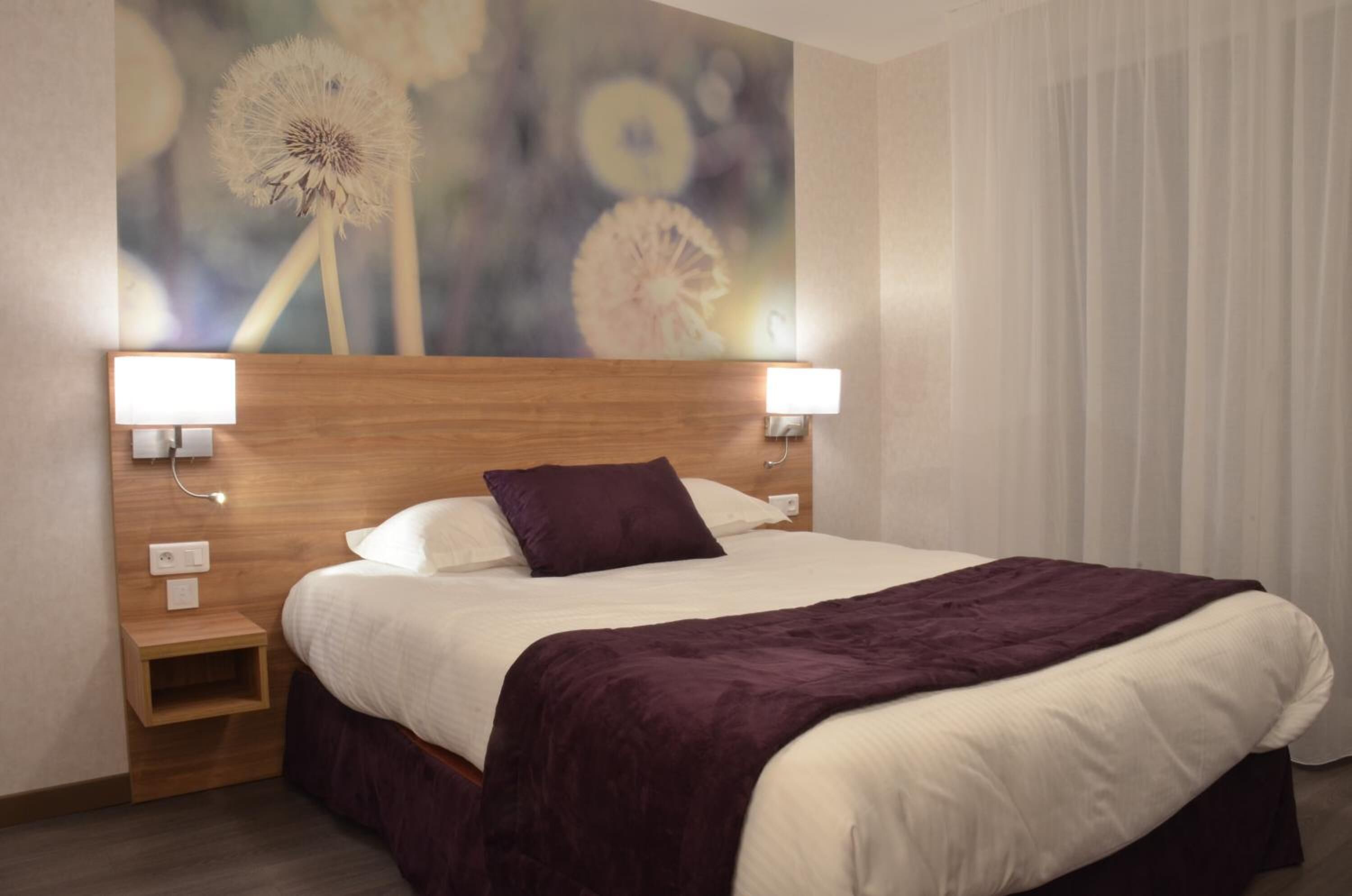 A hotel room with a large bed, two bedside lamps, a wooden headboard, and a wall mural of dandelions.