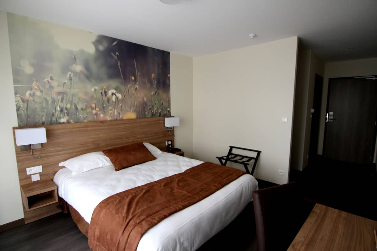 Habitación de hotel con una cama grande, un cabecero de madera, una mesita de noche, un escritorio y un cuadro en la pared.
