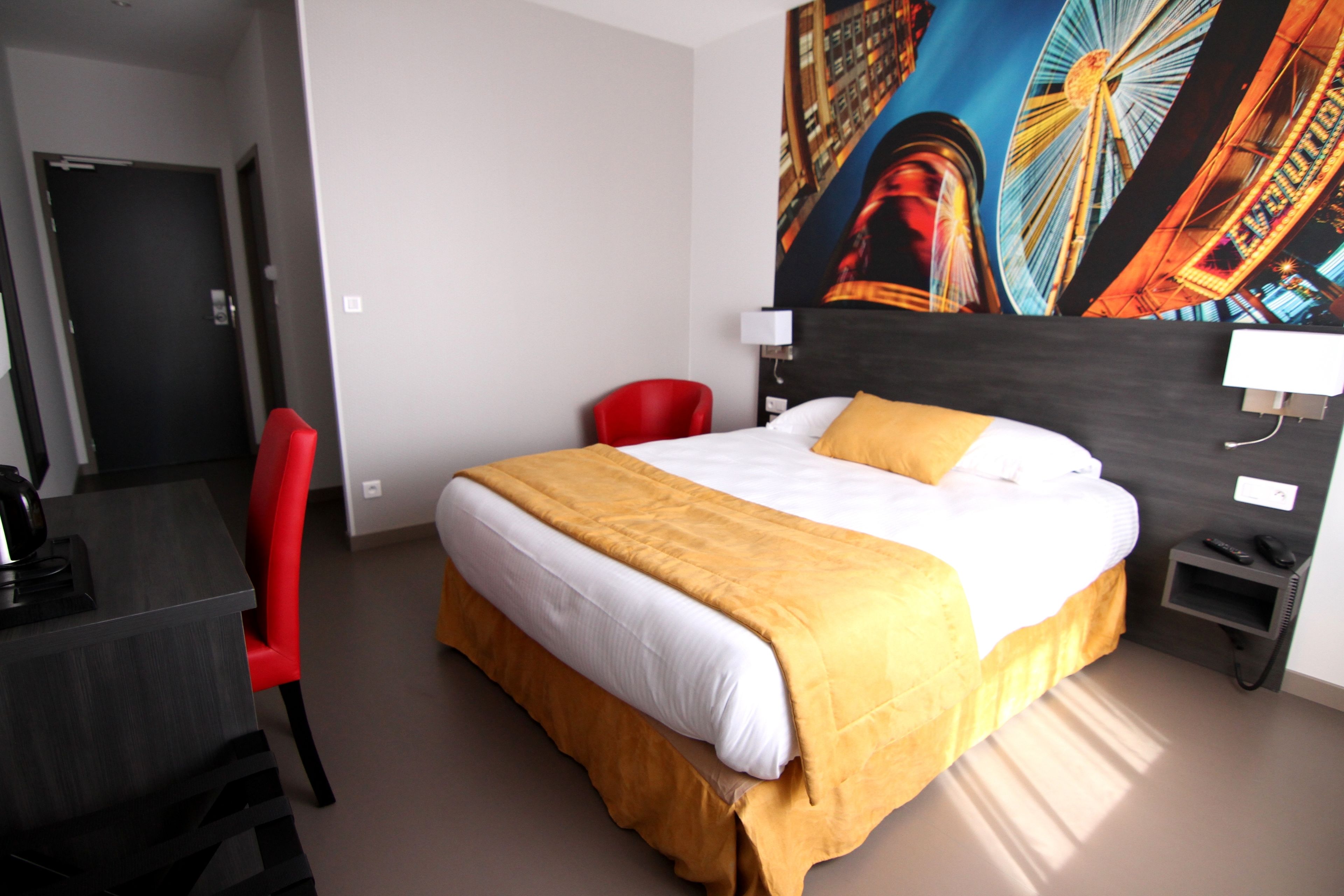 A hotel room with a bed, a desk, a chair, and a painting of a Ferris wheel.