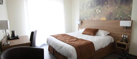 A hotel room with a large bed, a desk with a lamp, a chair, and a painting on the wall.