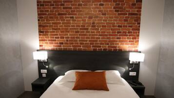 Ein Hotelzimmer mit einer Wand im Backsteinmuster, einem schwarzen Kopfteil, einem weißen Bett mit einem braunen Kopfkissen und zwei Nachttischen mit Lampen.