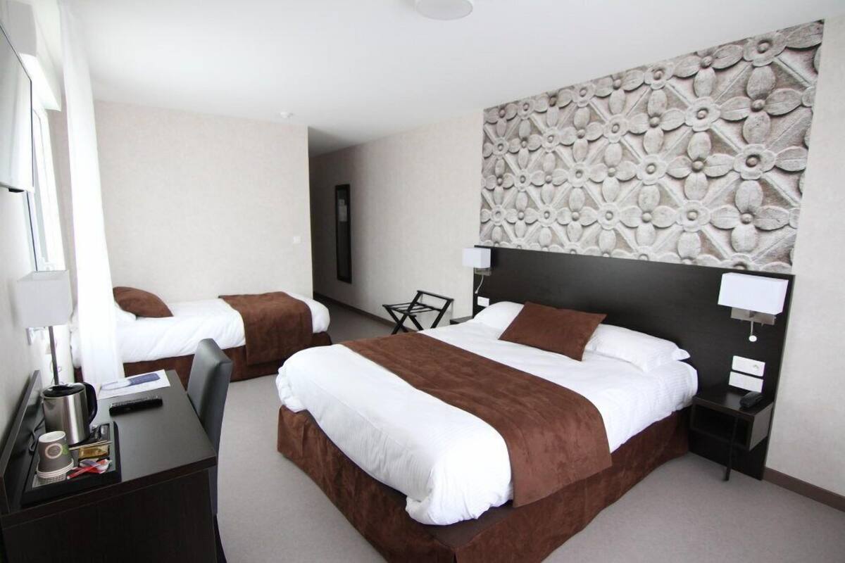 Habitación de hotel con dos camas, un escritorio, una silla, un panel decorativo en la pared y una mesita de noche con lámpara.