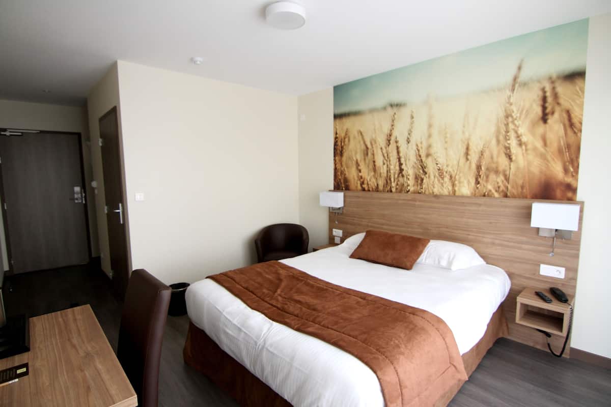 Habitación de hotel con una cama grande, cabecero de madera, un cuadro de campos de trigo, un escritorio y una silla.