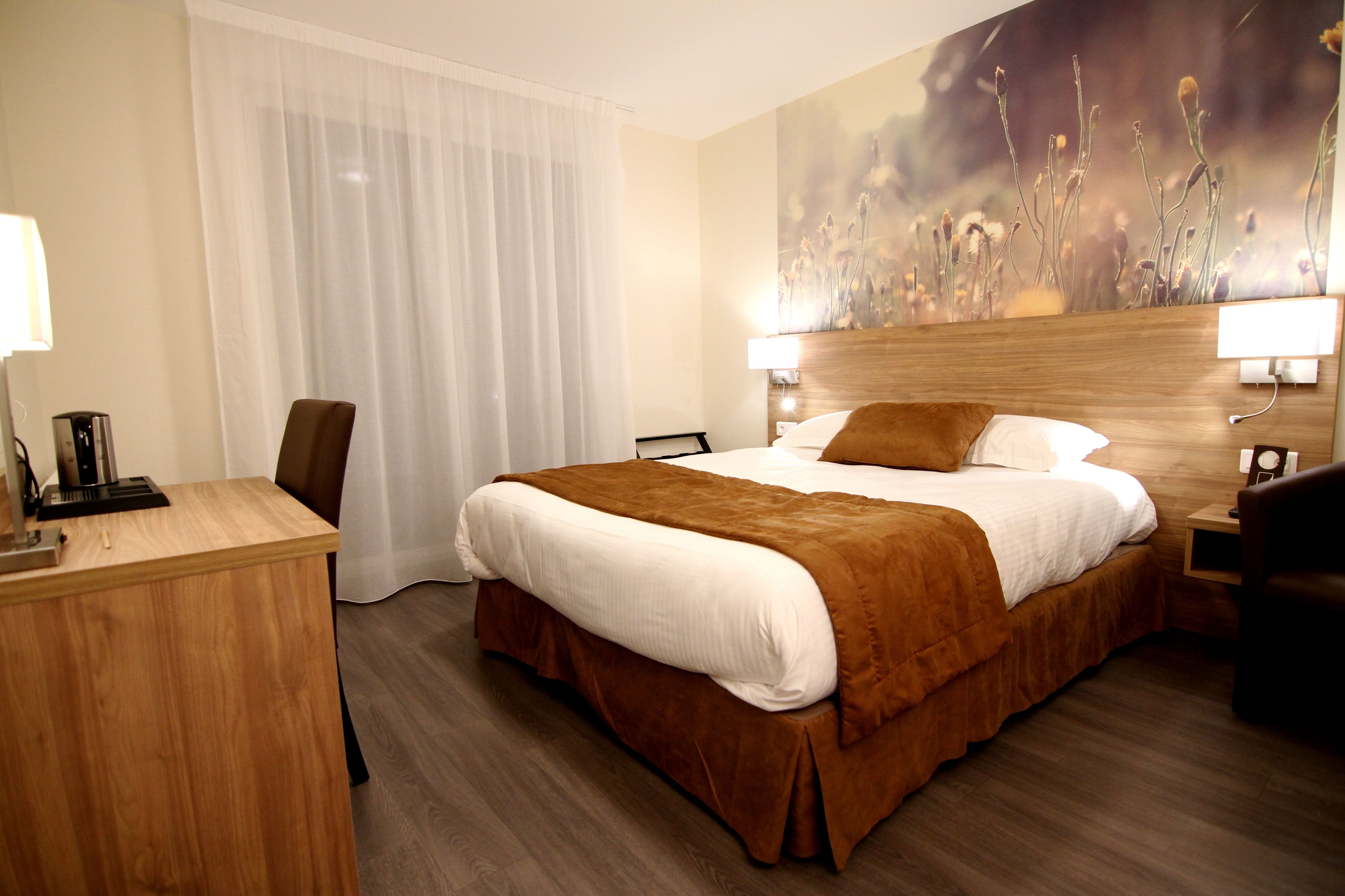 A hotel room with a large bed, a desk, a chair, and a nightstand with a lamp.