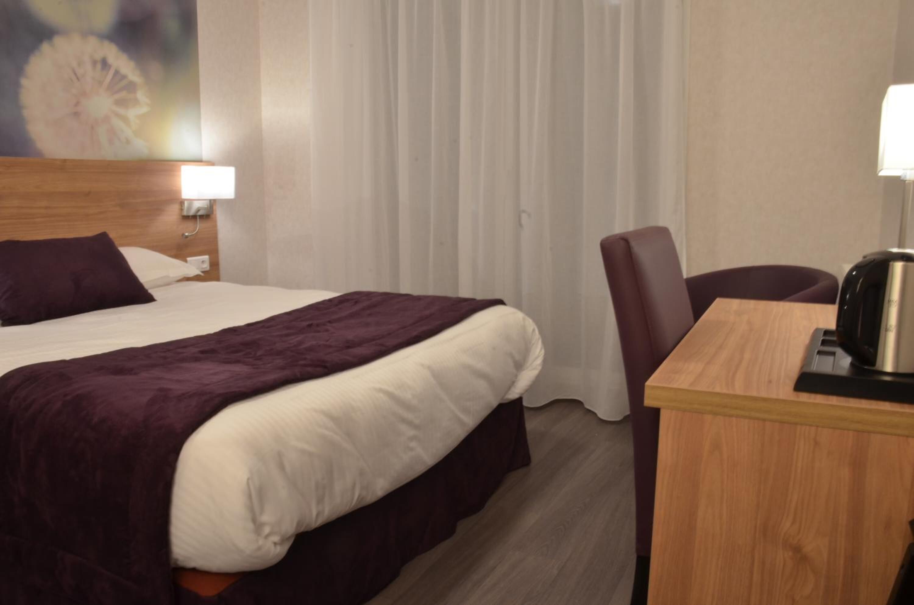 Een hotelkamer met een bed, een bureau met een waterkoker, en een stoel.