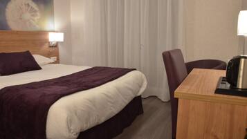 Een hotelkamer met een bed, een bureau met een waterkoker, en een stoel.