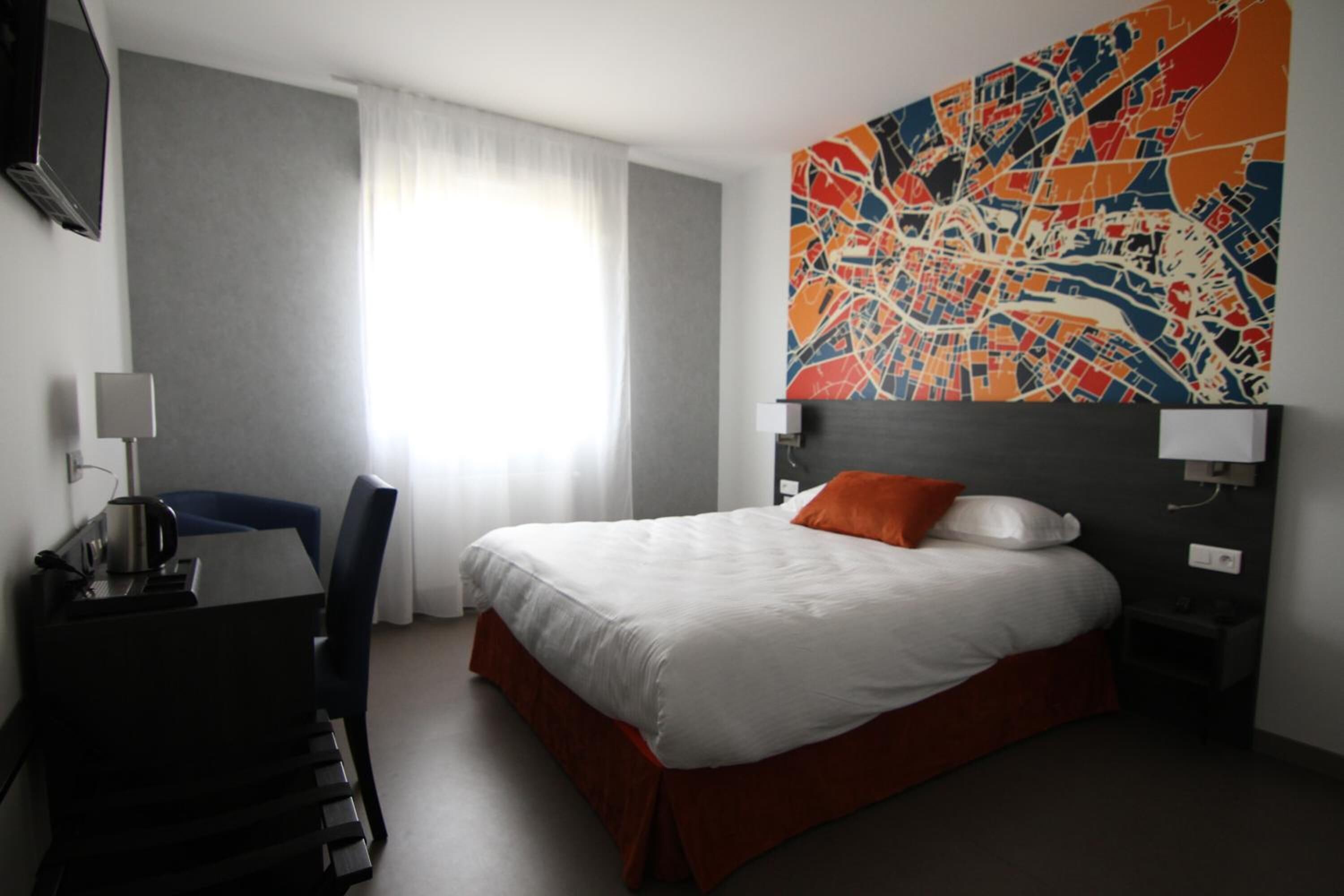 A hotel room with a large bed, a desk with a chair, a TV, and a colorful abstract painting on the wall.