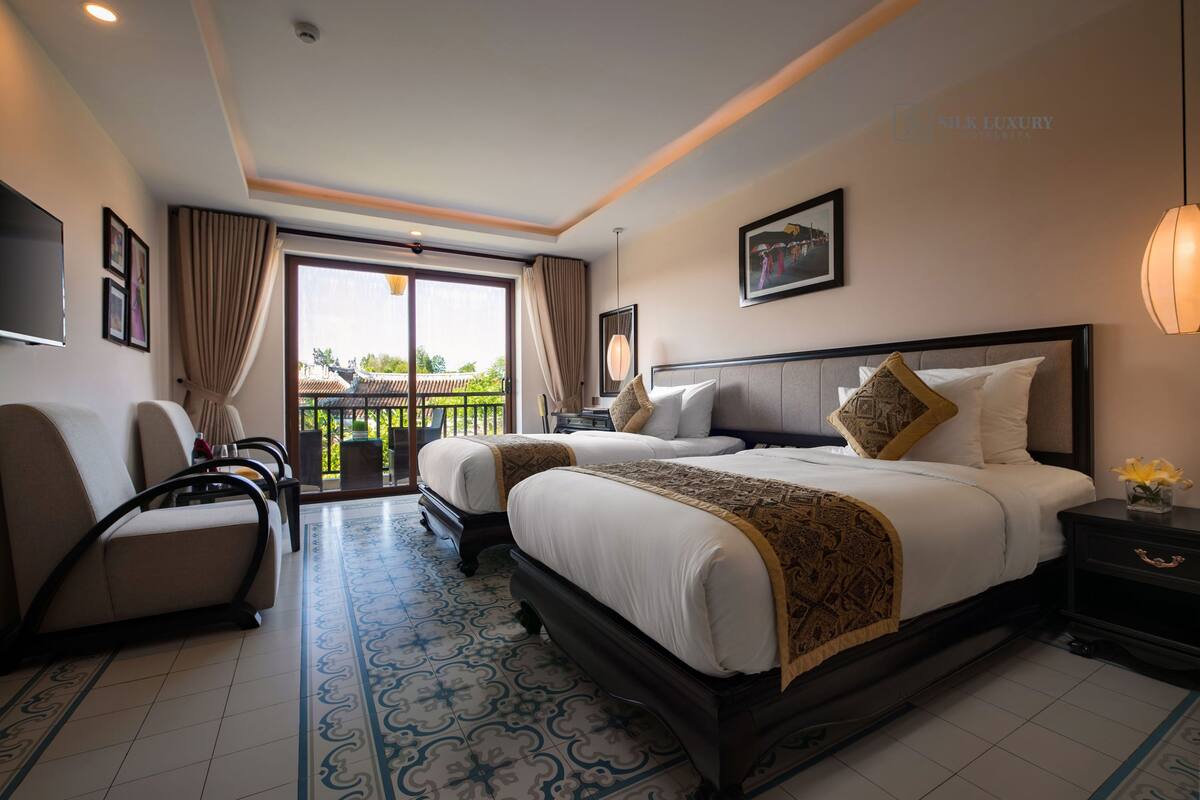A hotel room with two beds, a sofa, a TV, and a balcony with a view.