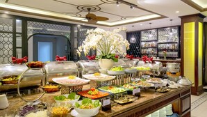 A buffet with various food options, a decorative flower centerpiece, and a bar area with glassware. - Silkotel Hoi An (Da Nang)