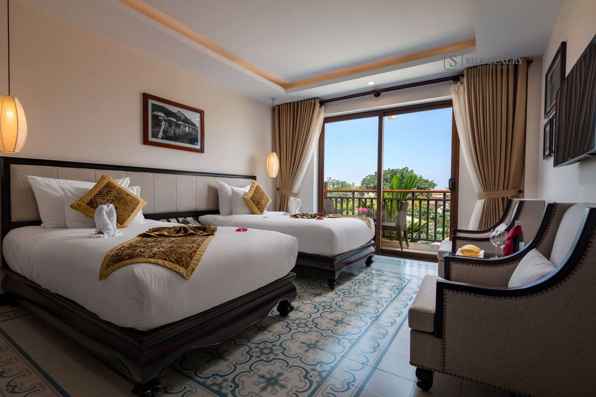 A hotel room with two beds, a balcony, and a seating area with a view.