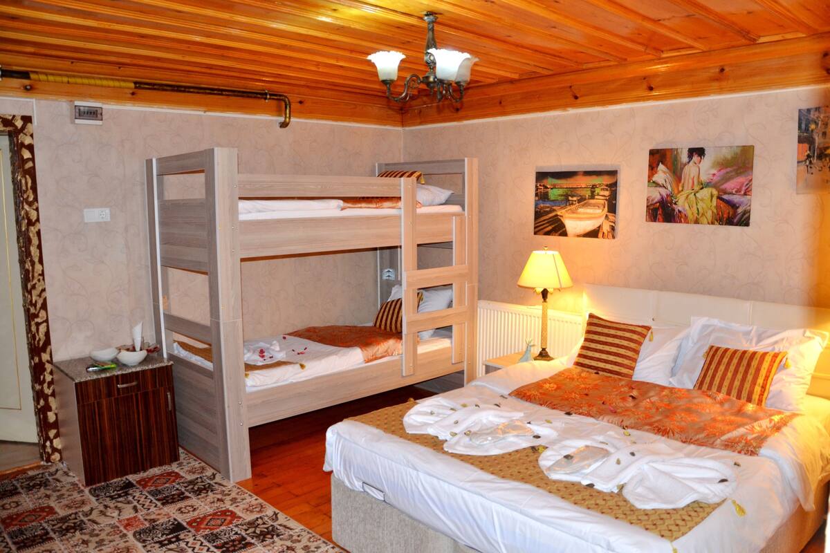 Una habitación con una cama individual, una litera, una mesita de noche, una lámpara y un cuadro en la pared.