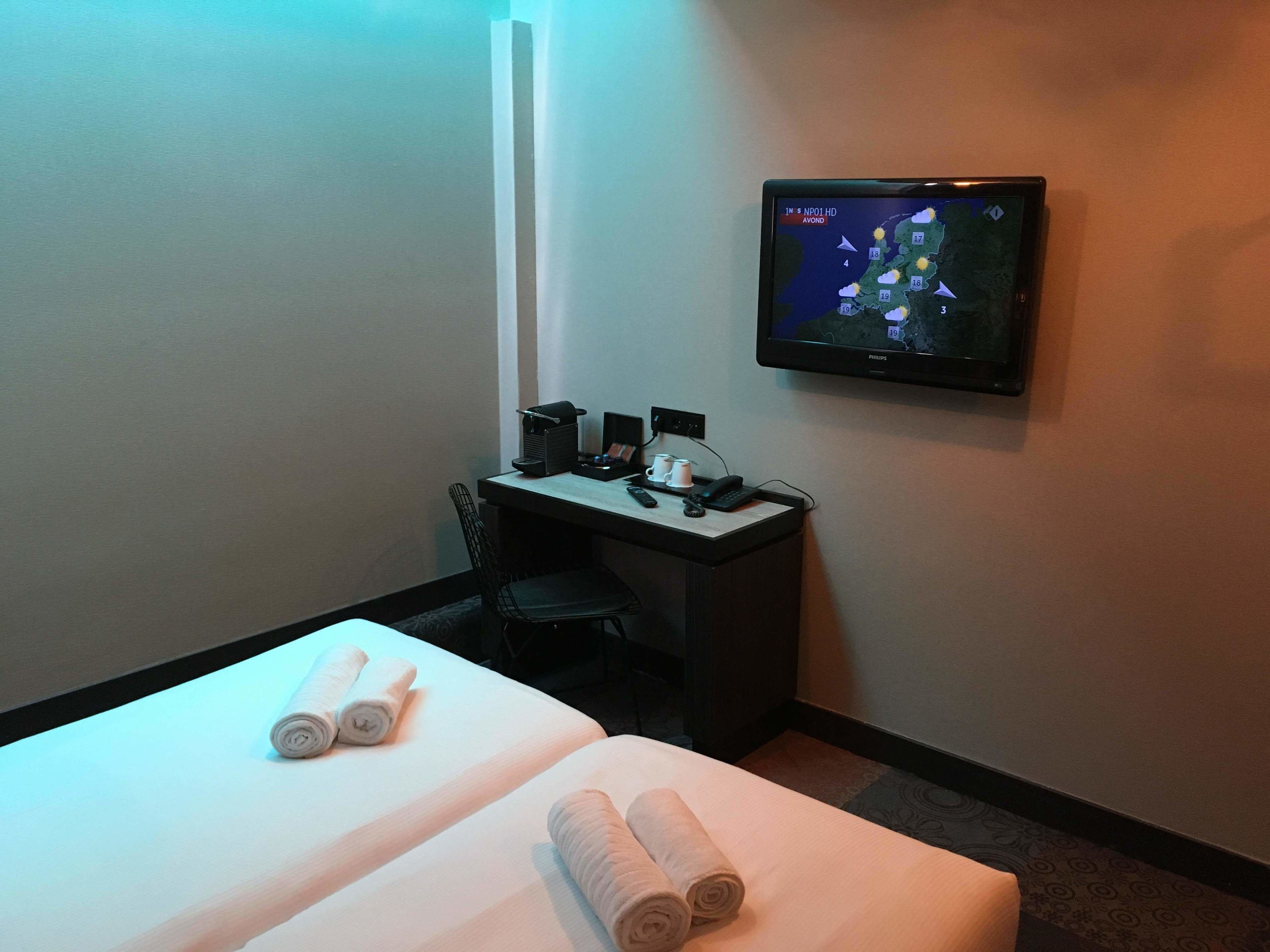 A hotel room with a bed, a desk, a chair, a television, and a coffee maker.