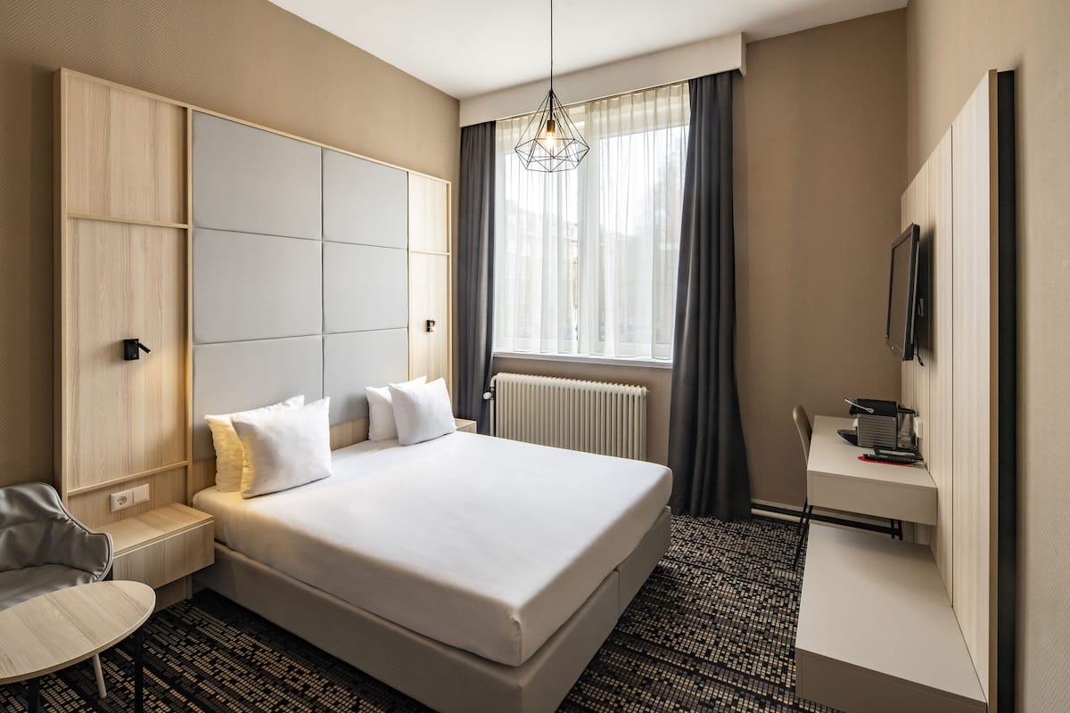 Ett modernt hotellrum med en stor säng, ett skrivbord, en stol och en TV.