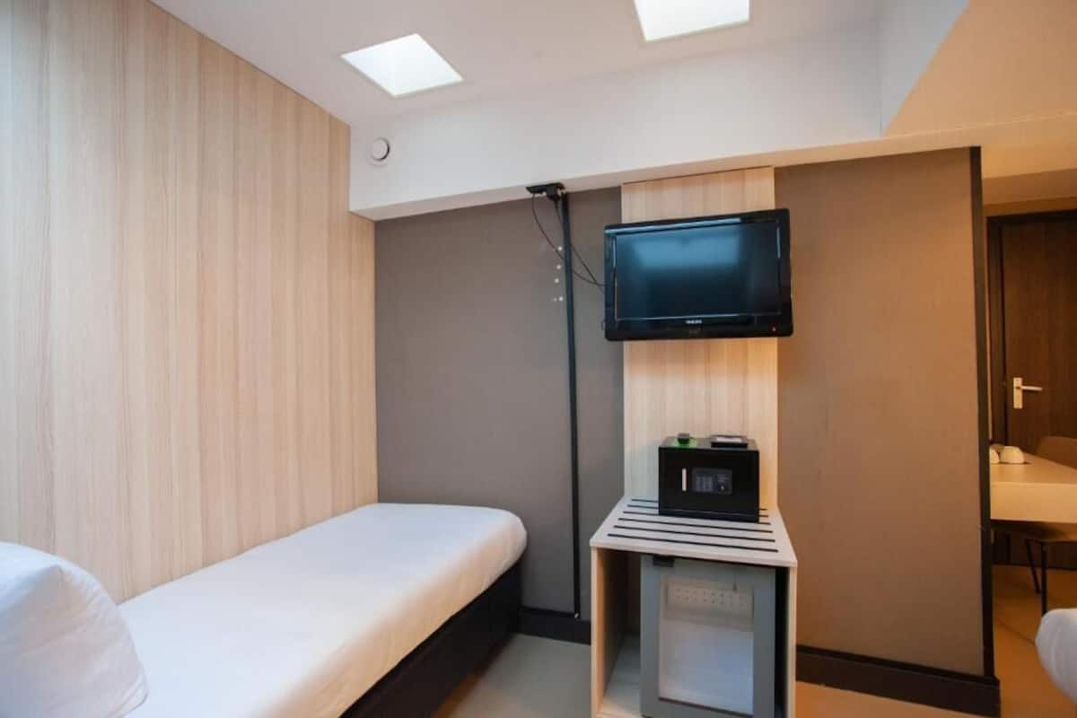 Ett hotellrum med en säng, en tv som är monterad på en träpanel och ett litet skåp med en mikrovågsugn.
