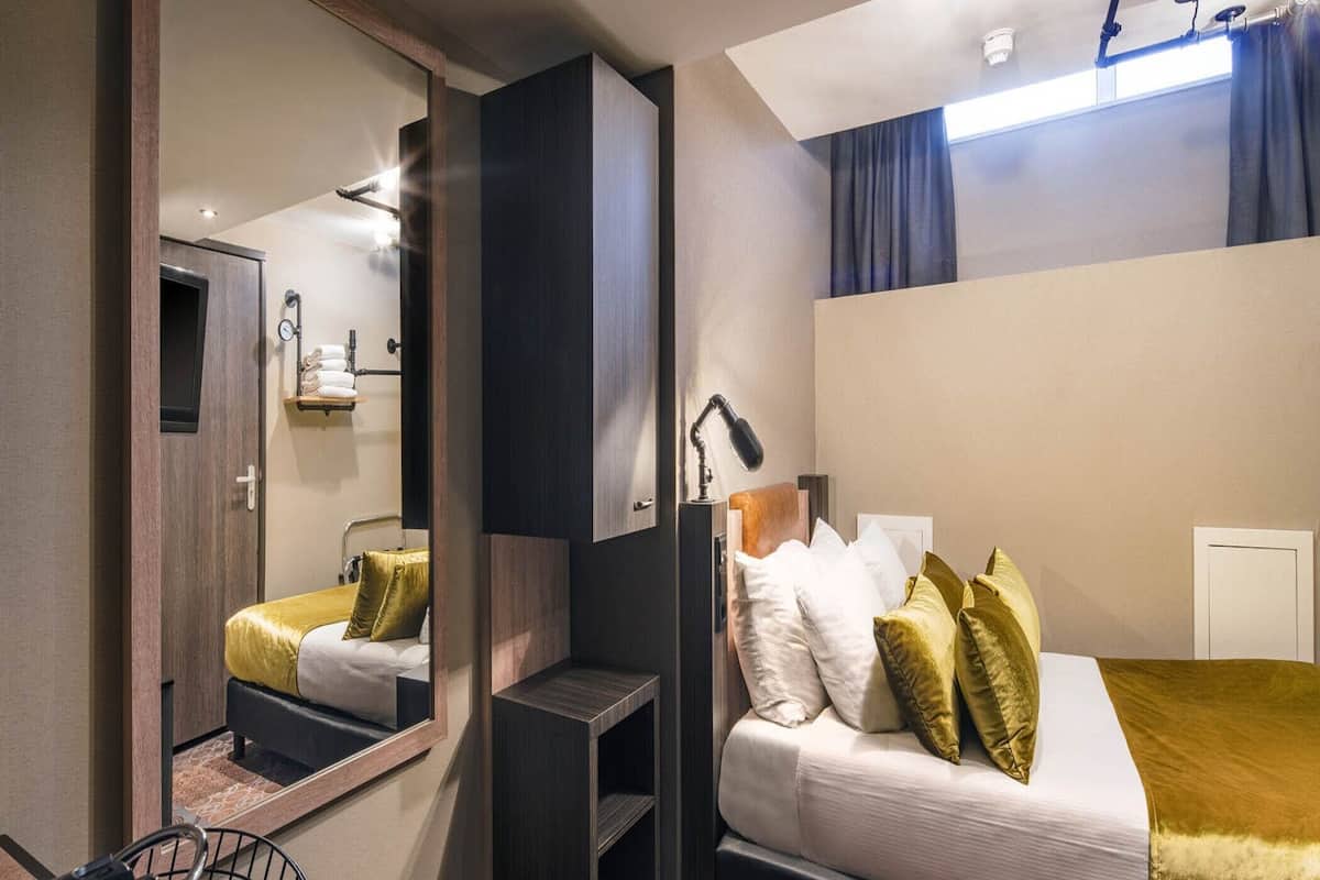 Ett modernt hotellrum med en säng, ett skrivbord, en stol, en spegel och ett fönster med gardiner.