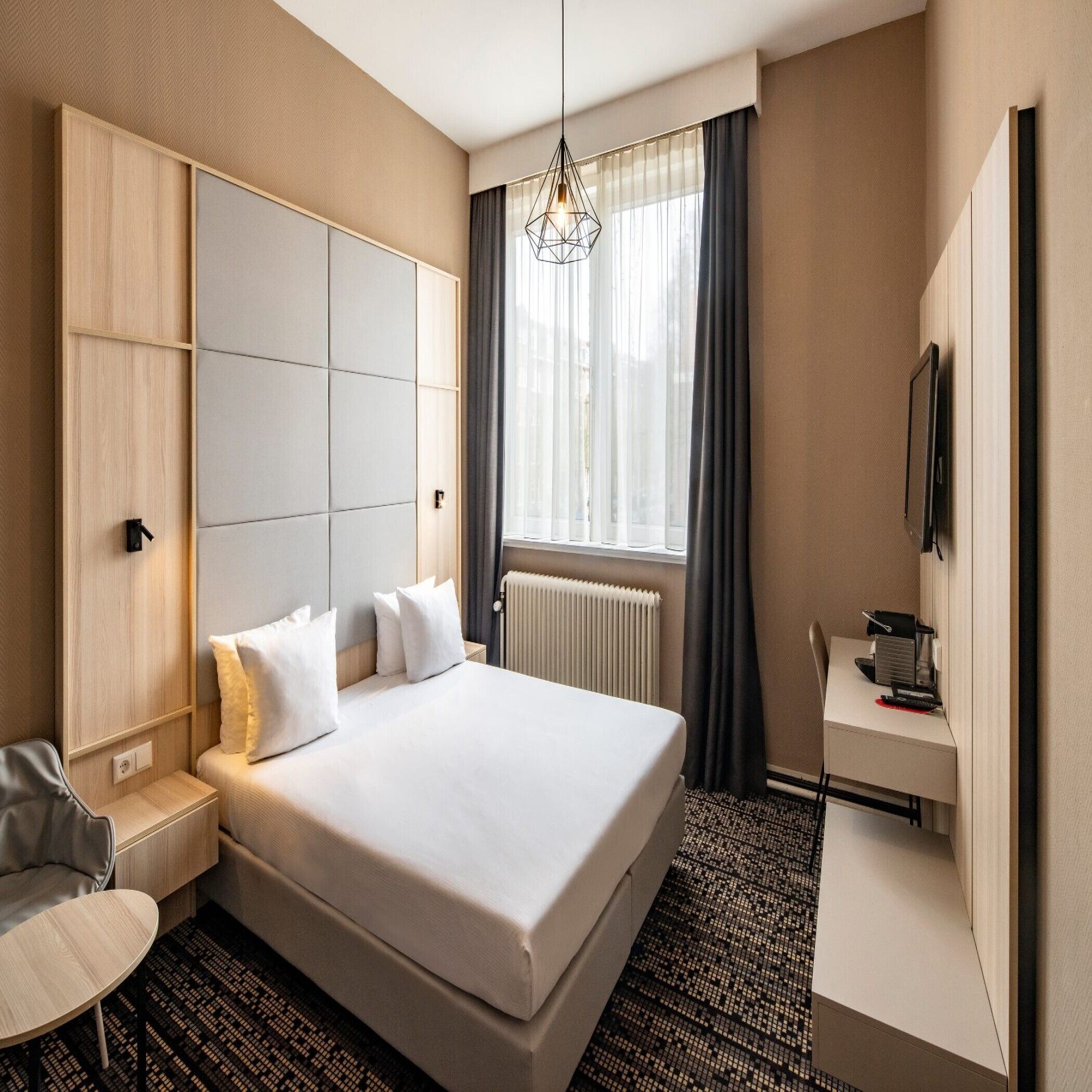 A hotel room with a large bed, a desk, a chair, a TV, and a window with curtains.