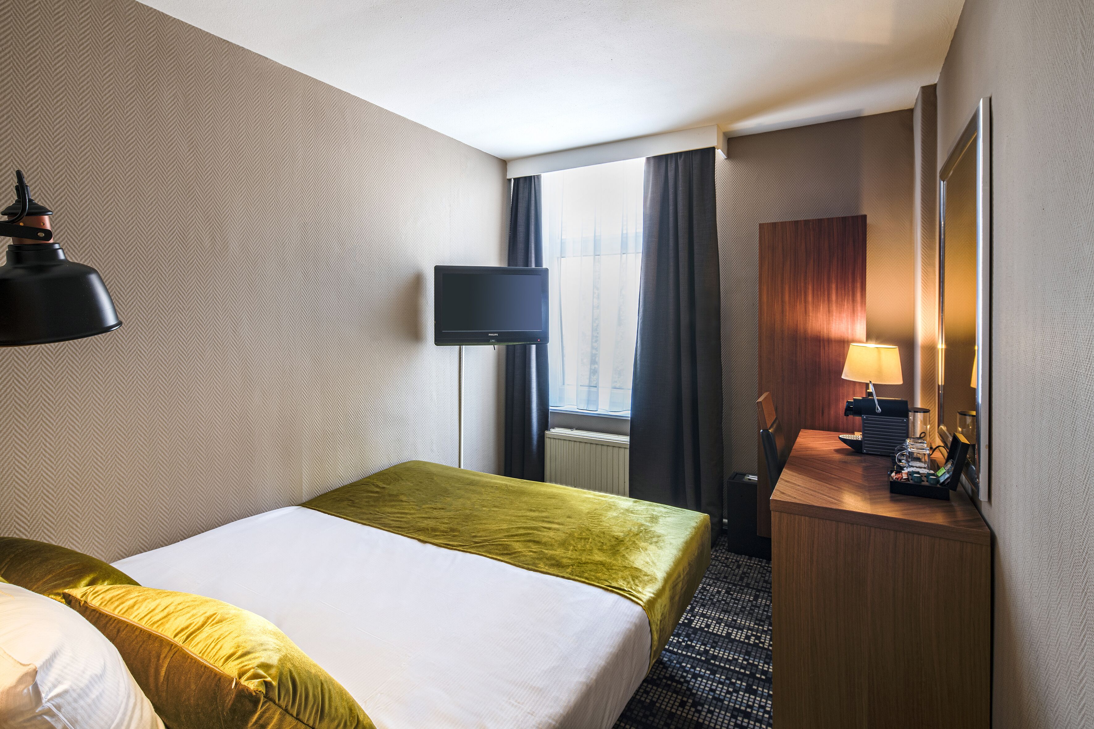 A hotel room with a bed, a desk, a television, and a window with curtains.