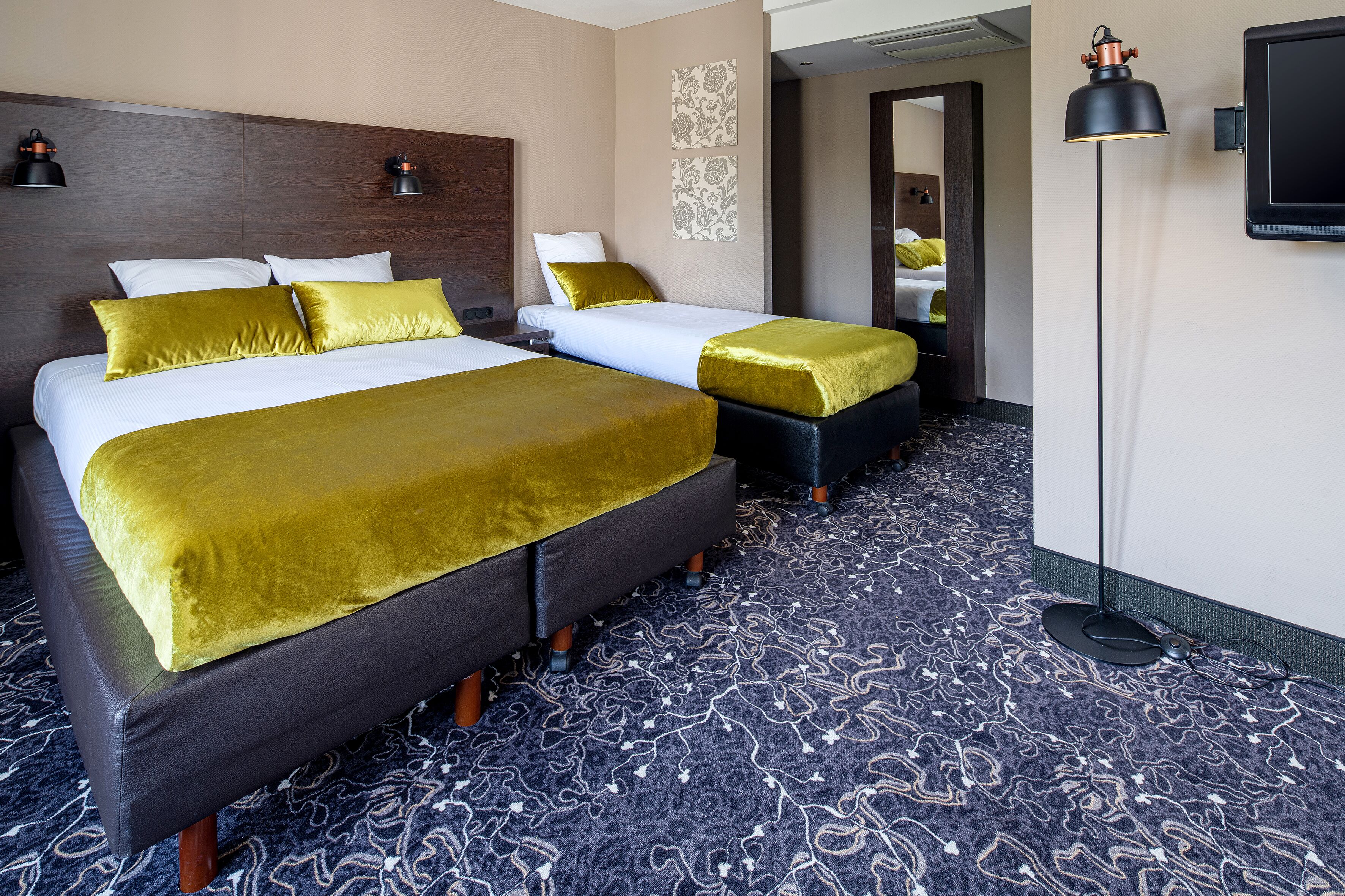 A hotel room with two beds, a large mirror, and a floor lamp.