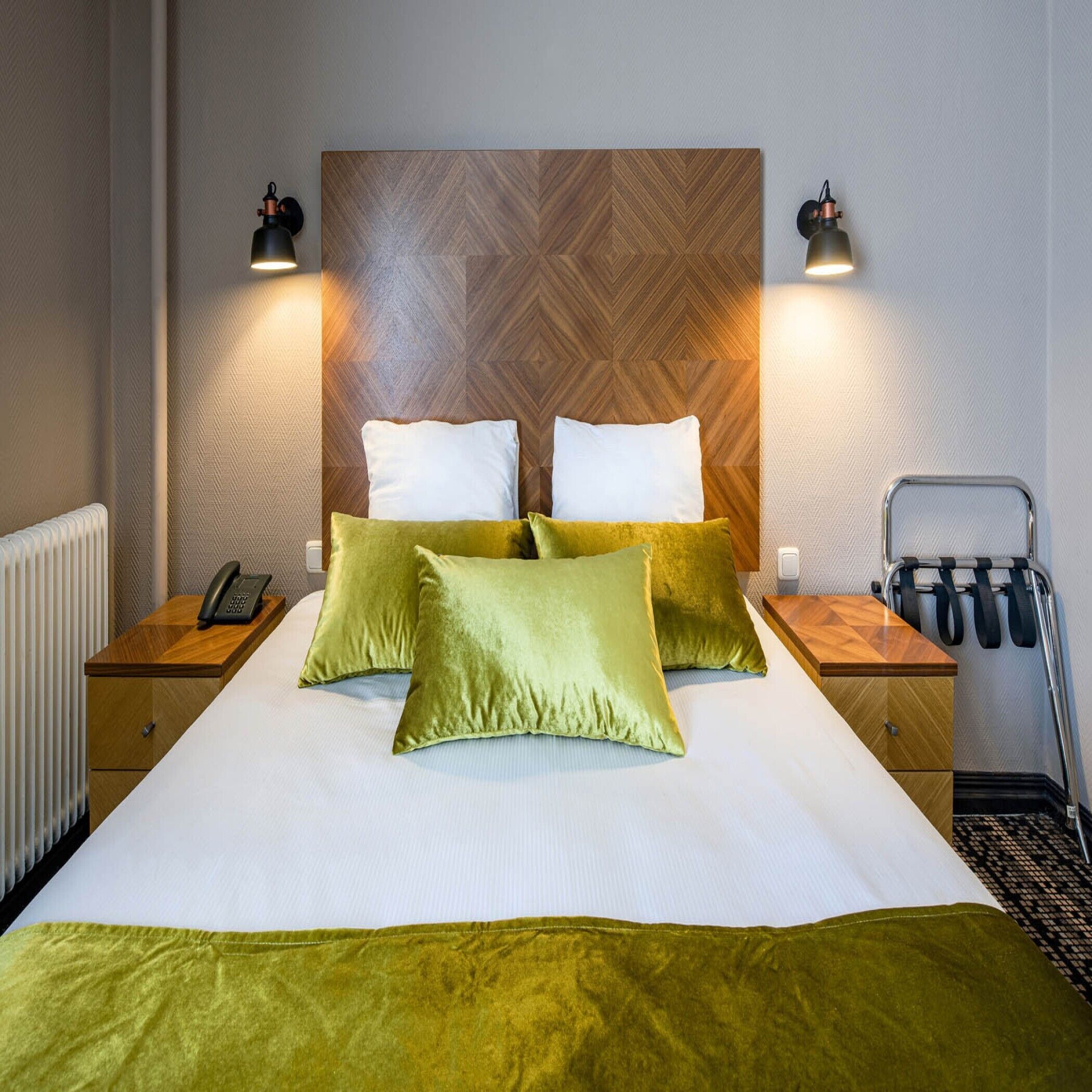 A hotel room with a large bed, two bedside tables, a wooden headboard, and two wall-mounted lamps.