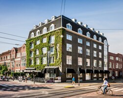 A hotel with a modern design, featuring a mix of brick and glass facade, and a prominent ivy-covered corner.