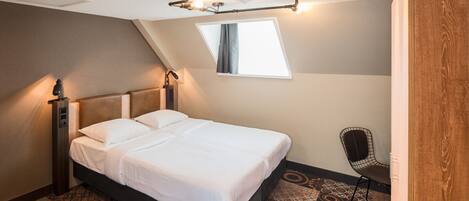 A modern hotel room with a neatly made bed, a chair, and a unique ceiling light fixture.