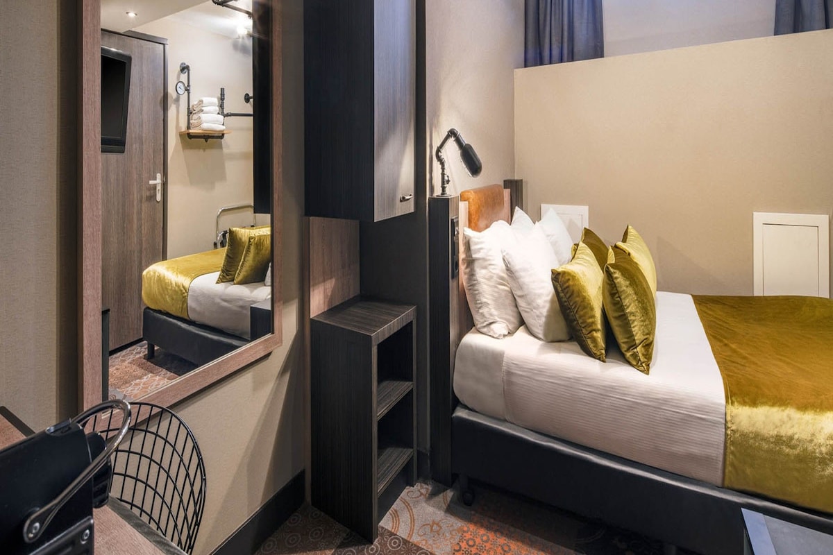 Una habitación de hotel moderna con cama, escritorio, silla, espejo y ventana con cortinas.