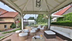 An outdoor patio with wicker furniture, a glass table, and a white umbrella. - Hotel Gödecke (Sarstedt)