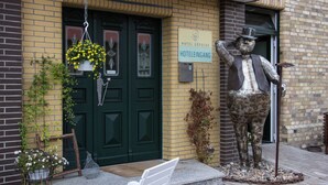 A hotel entrance with a green door, a hanging flower basket, and a statue of a man with a hat. - Hotel Gödecke (Sarstedt)