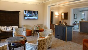 A hotel lobby with a sofa, armchairs, a small round table, a television mounted on the wall, and a bar area. - Hotel Gödecke (Sarstedt)