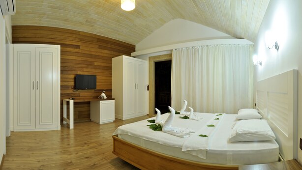 A bedroom with a wooden ceiling, a bed with white bedding, a desk with a television, and a wardrobe. - Apella Hotel (Kemer)