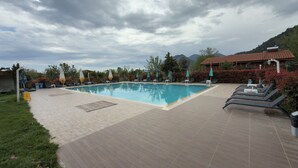 A swimming pool with lounge chairs and umbrellas, surrounded by greenery and a mountainous backdrop. - Apella Hotel (Kemer)