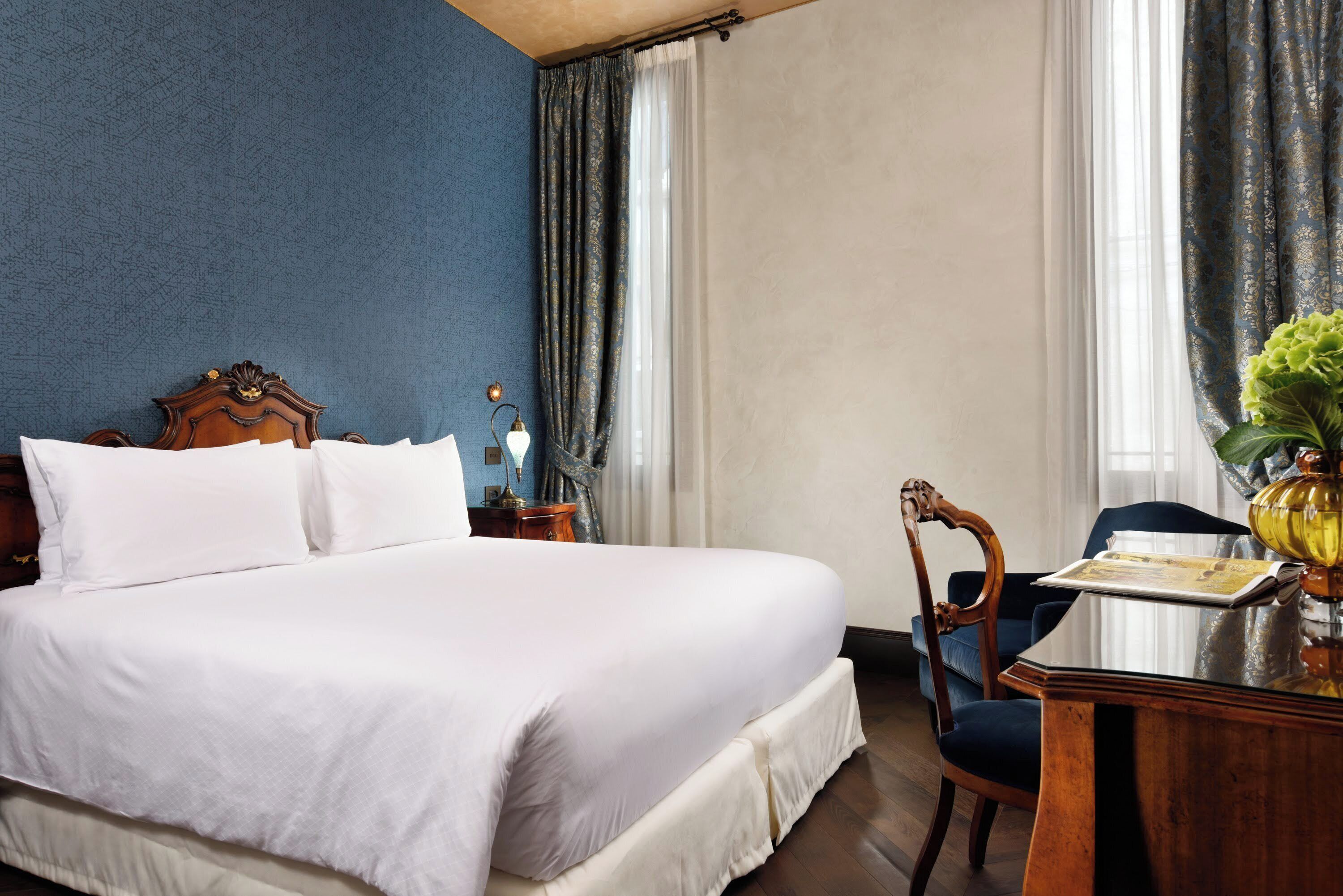 Une chambre d’hôtel avec un grand lit, une table de chevet en bois, un bureau avec une chaise et une fenêtre avec des rideaux.