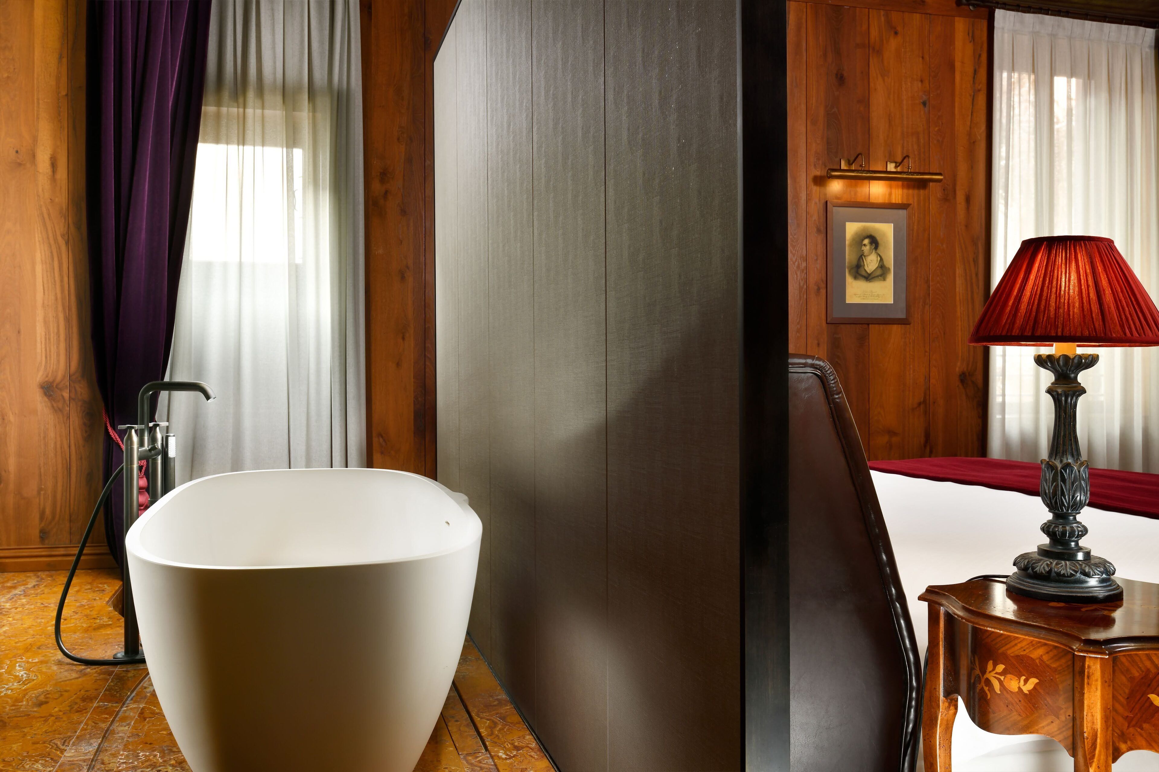 A modern bathroom with a large white bathtub, wooden paneling, and a red lamp on a wooden side table.