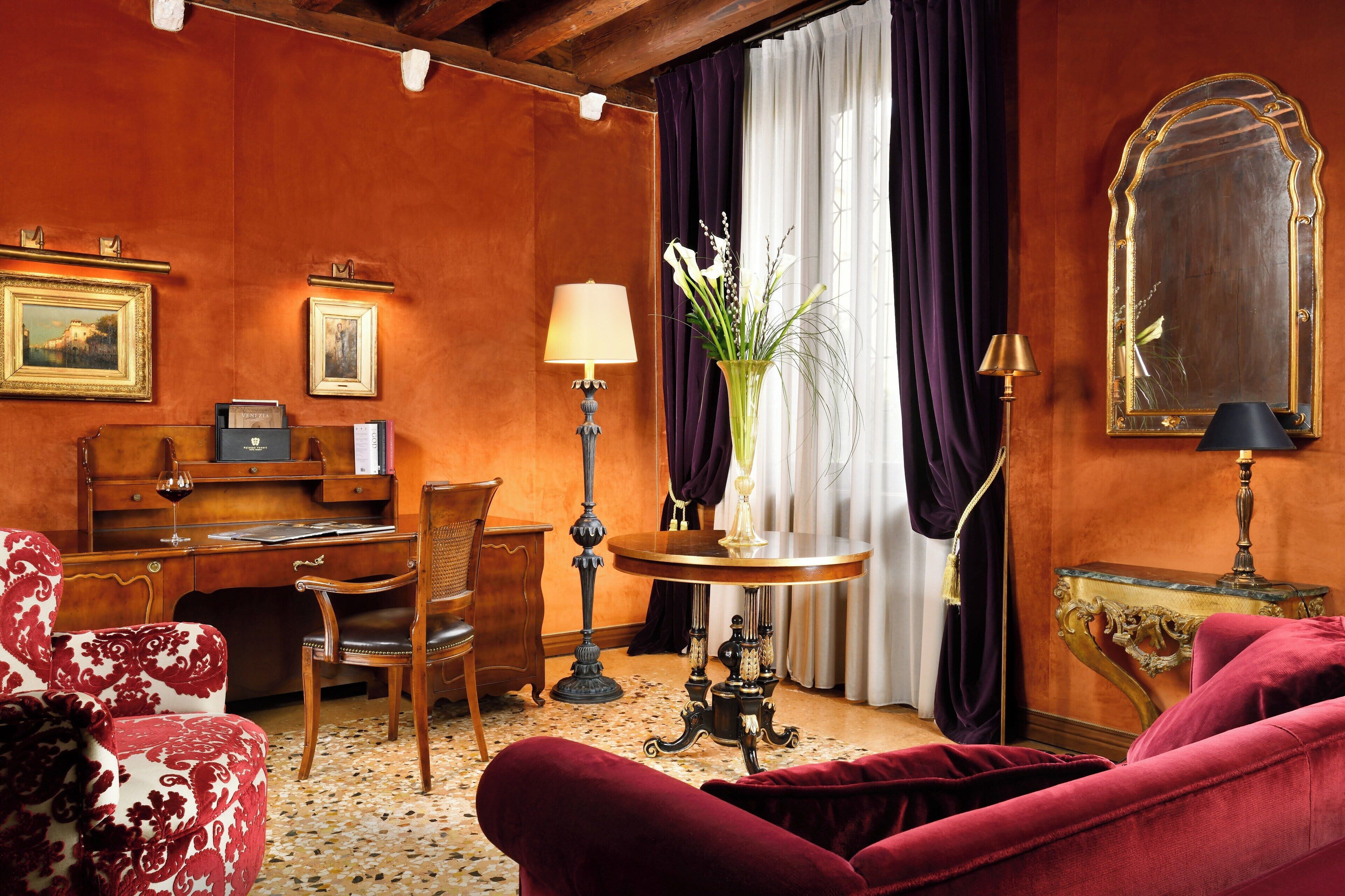 Una habitación con un escritorio de madera, una silla, un sofá rojo, una mesa con un florero y un espejo.