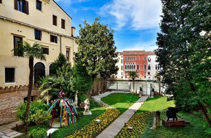 Un cortile con una statua, una palma e un vialetto che conduce a un edificio con facciata rossa.