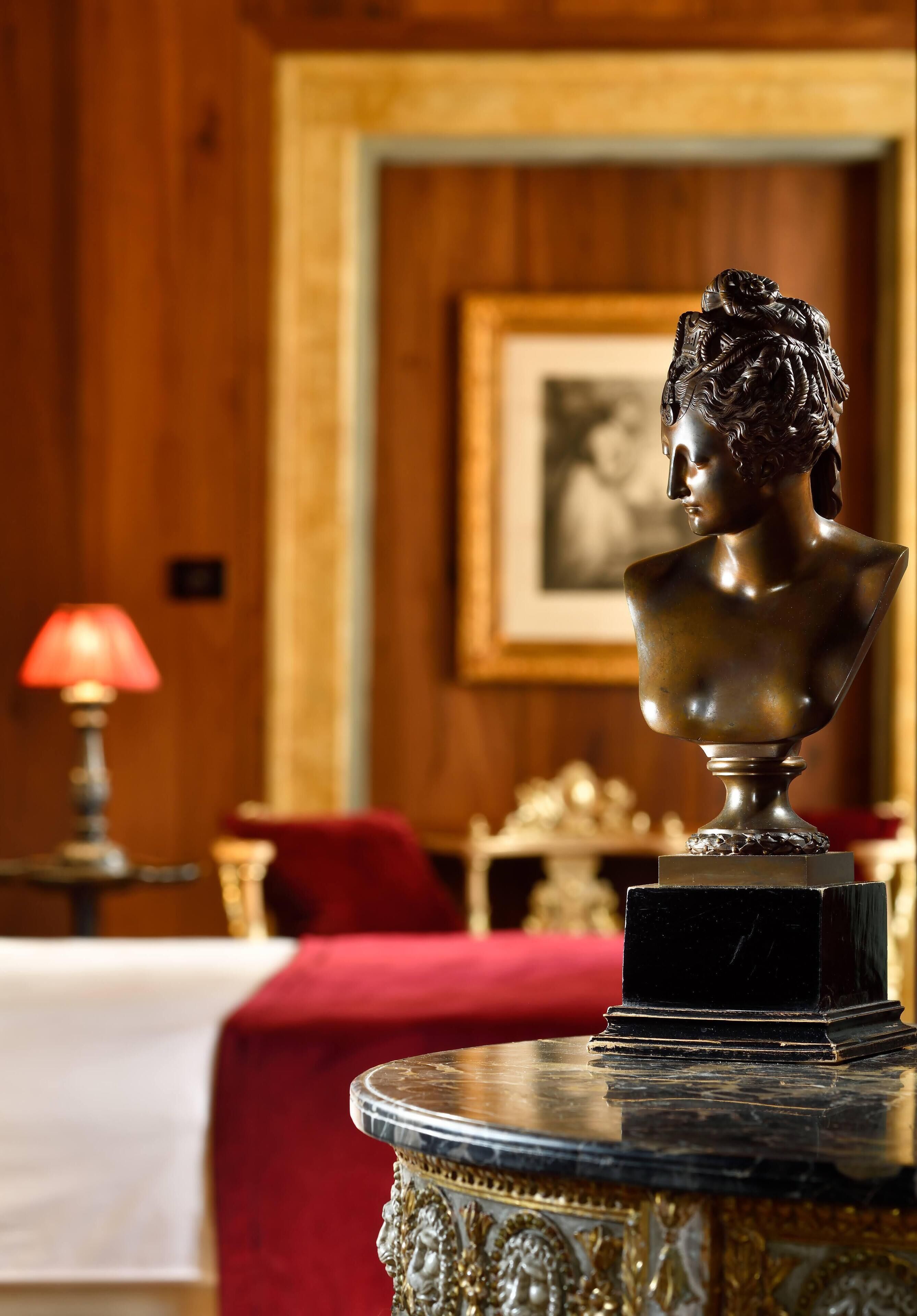 Un busto sobre un pedestal de mármol en una habitación con paneles de madera y un cuadro enmarcado en la pared.