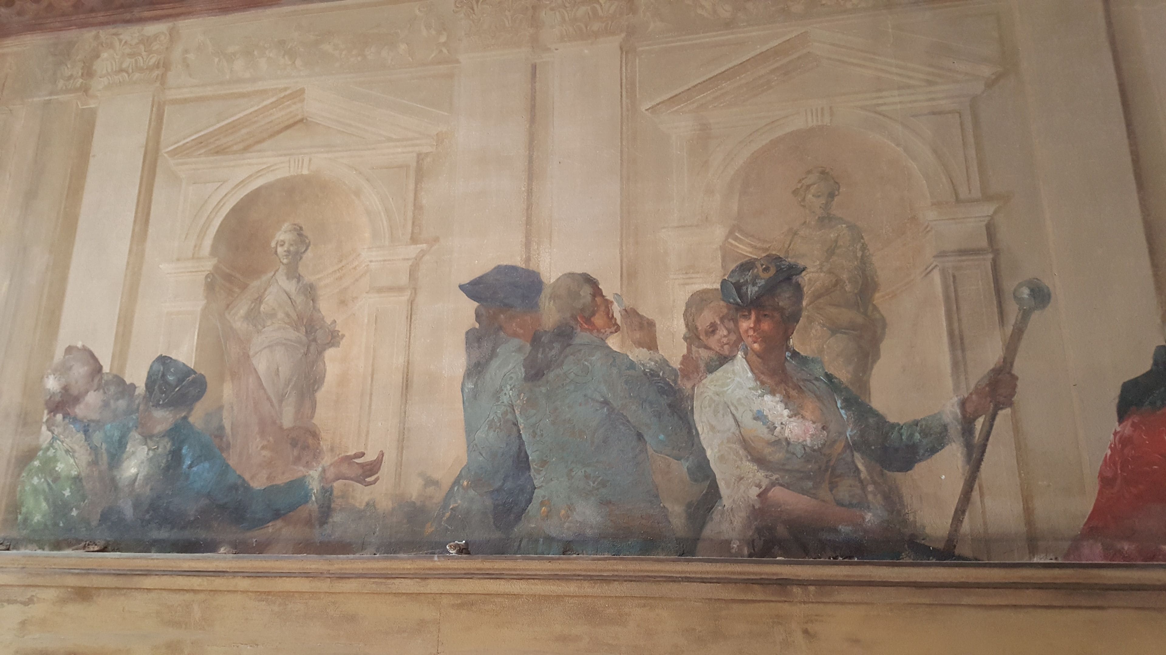A classical fresco mural with figures in historical attire, set against a backdrop of architectural columns and arches.