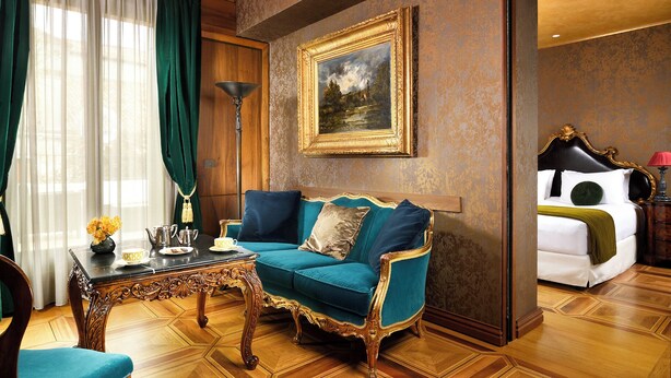Une pièce avec un canapé de couleur turquoise, une table basse en bois, un tableau accroché au mur et un lit avec une tête de lit noire.