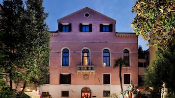 Un edificio grande de color rosa con una entrada central, ventanas arqueadas y un balcón.