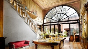 A grand staircase with a red sofa, a marble table with flowers, and a large arched window.