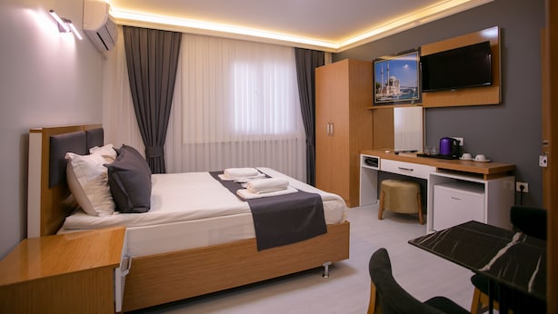 Moderni hotellihuone, jossa on sänky, työpöytä, tuoli ja seinälle asennettu taulutelevisio.