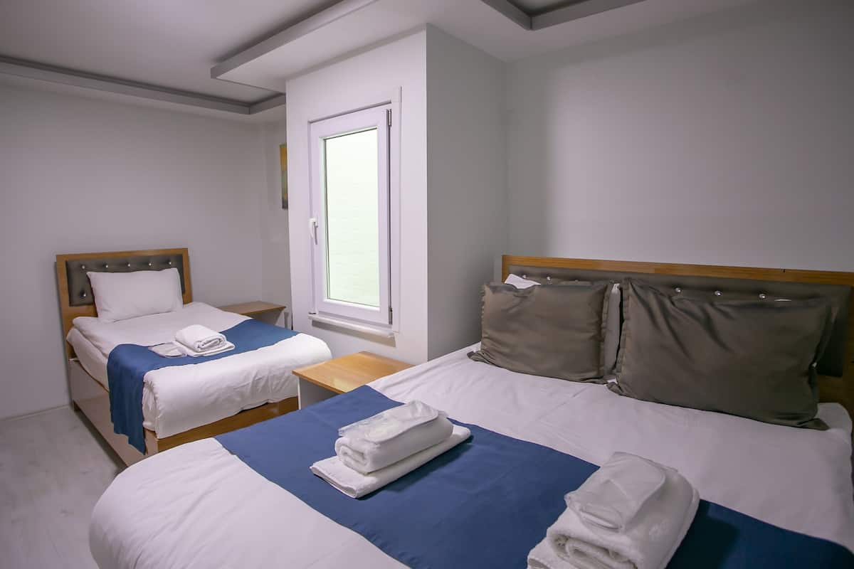 Habitación de hotel con dos camas individuales, cabecera de madera, una ventana y una mesita de noche pequeña.