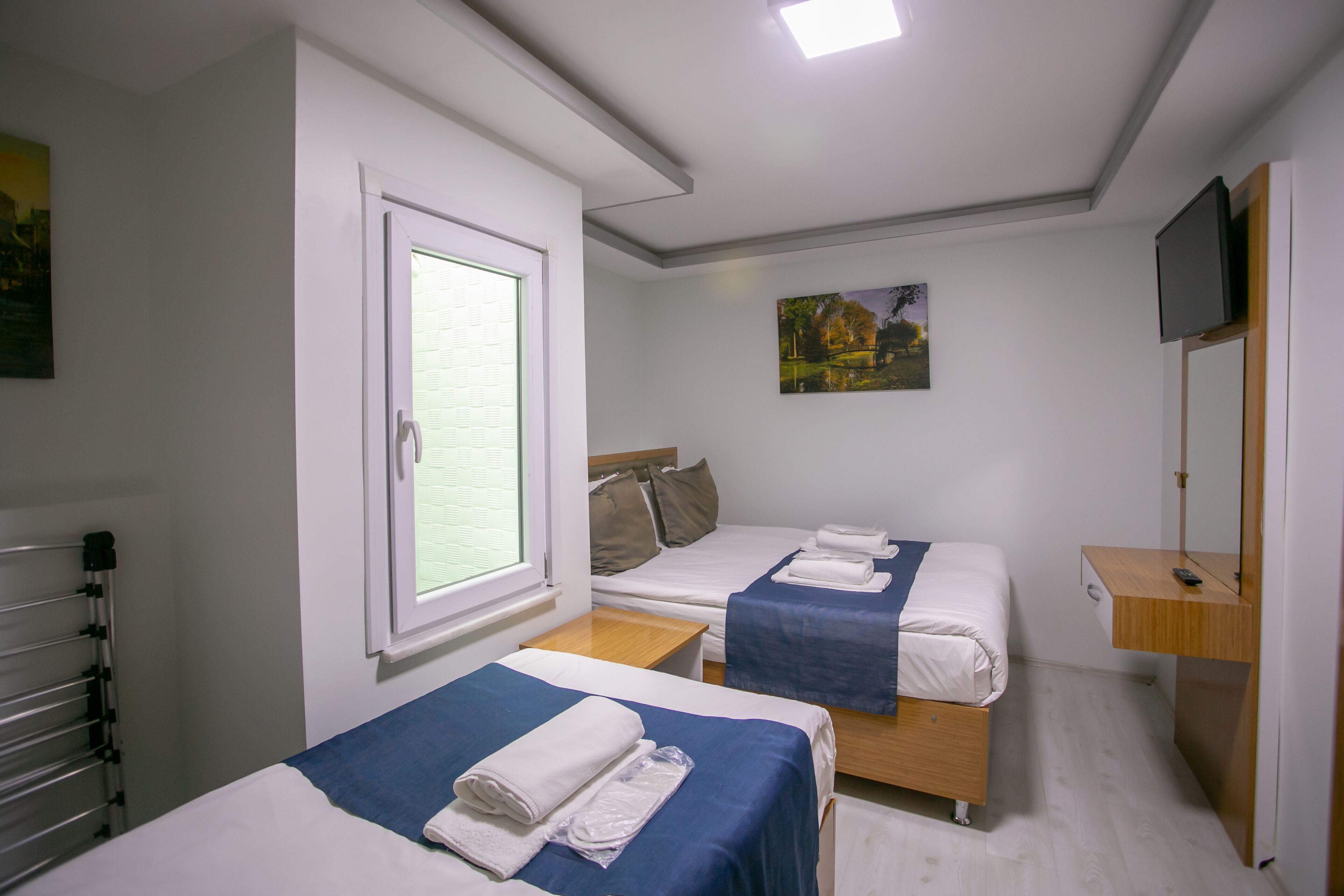 Habitación de hotel con dos camas, una ventana, un cuadro, un televisor y un escritorio de madera.