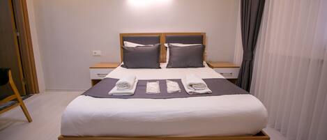 A neatly made bed with pillows, a bedside table, a wall-mounted air conditioner, and a curtain.