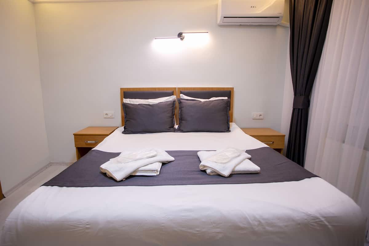 Una cama bien hecha con dos almohadas, una mesita de noche y un equipo de aire acondicionado en la pared.