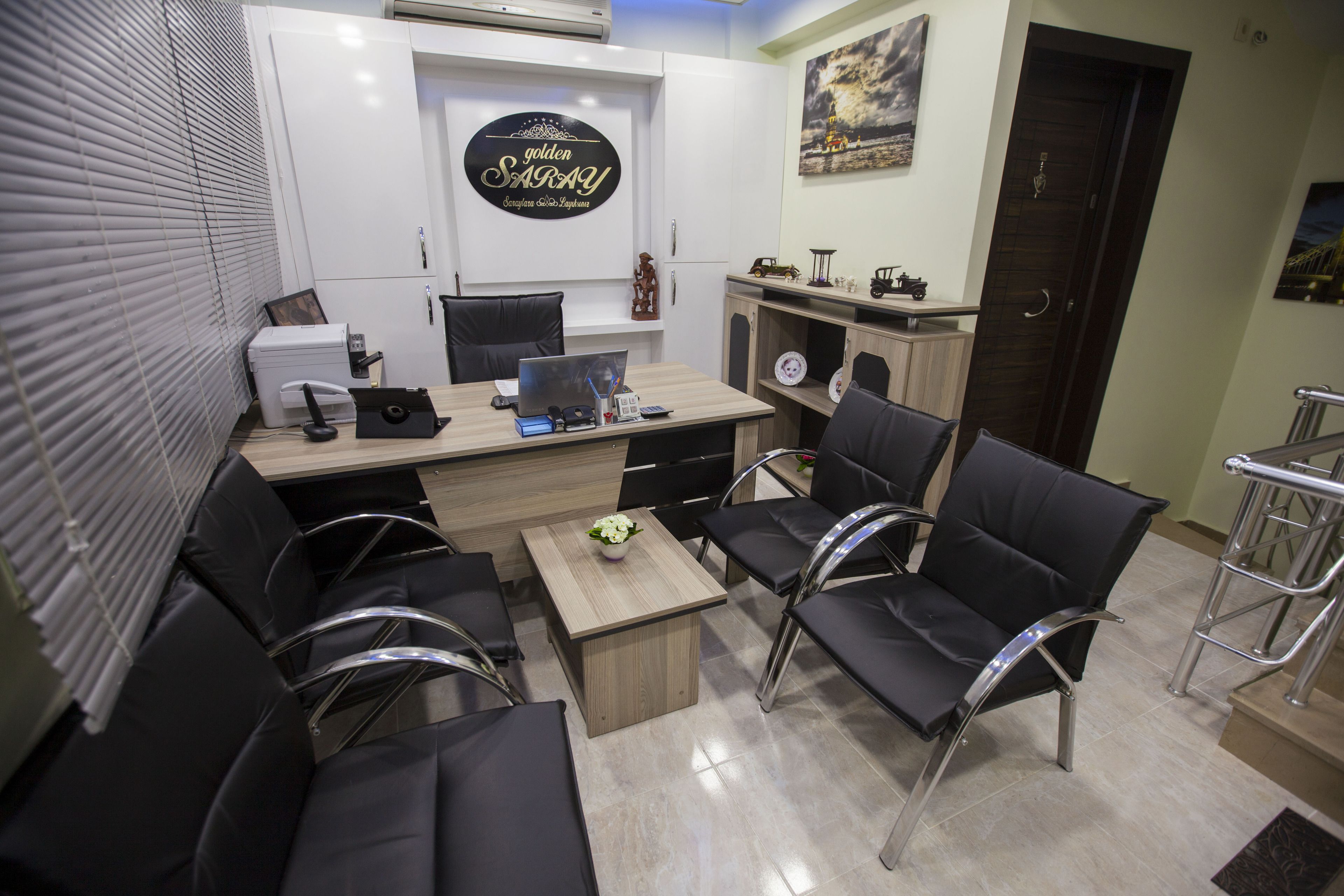 Un bureau moderne avec un bureau, des chaises et un ordinateur. Il y a un panneau sur le mur et une porte à l’arrière-plan.