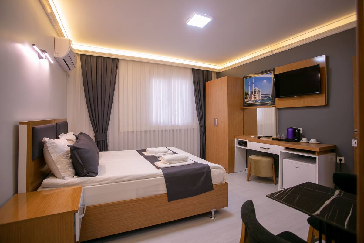 Una habitación de hotel moderna con cama, escritorio, silla, televisor y una kitchenette pequeña.